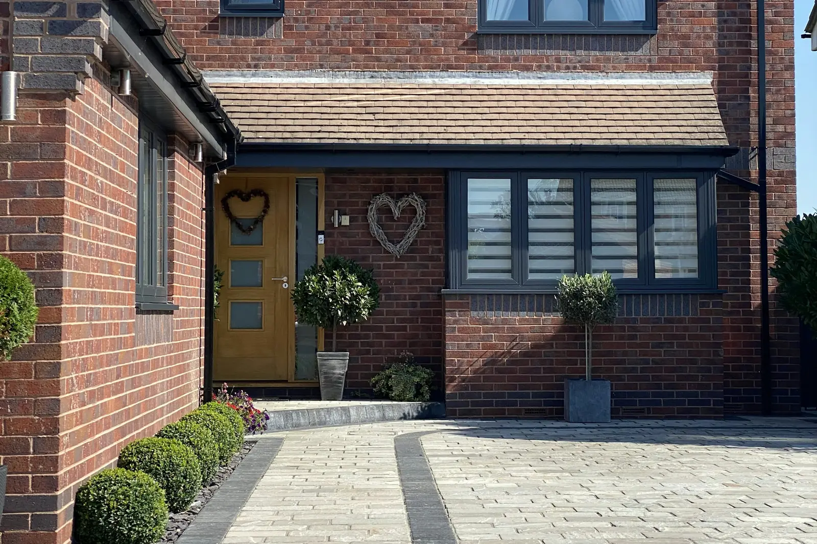 Block paved driveway in front of a red brick detached house with planted borders