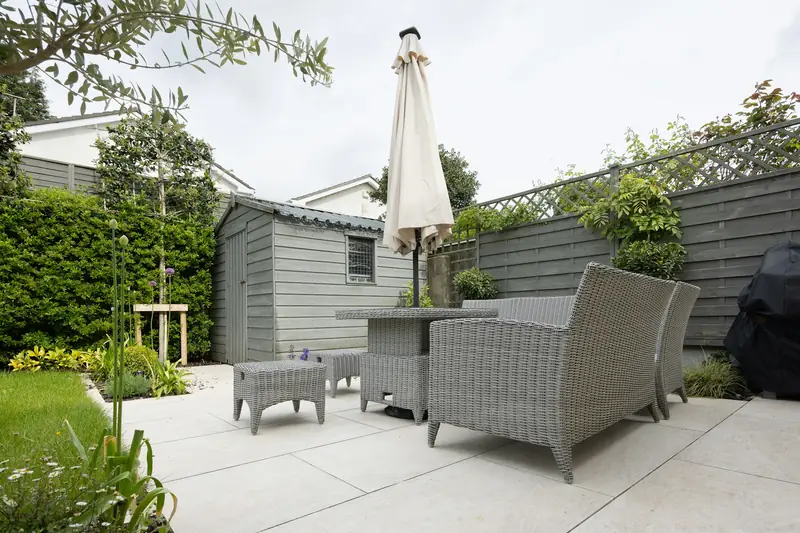 Paved patio with garden furniture, parasol and planting in a British back garden